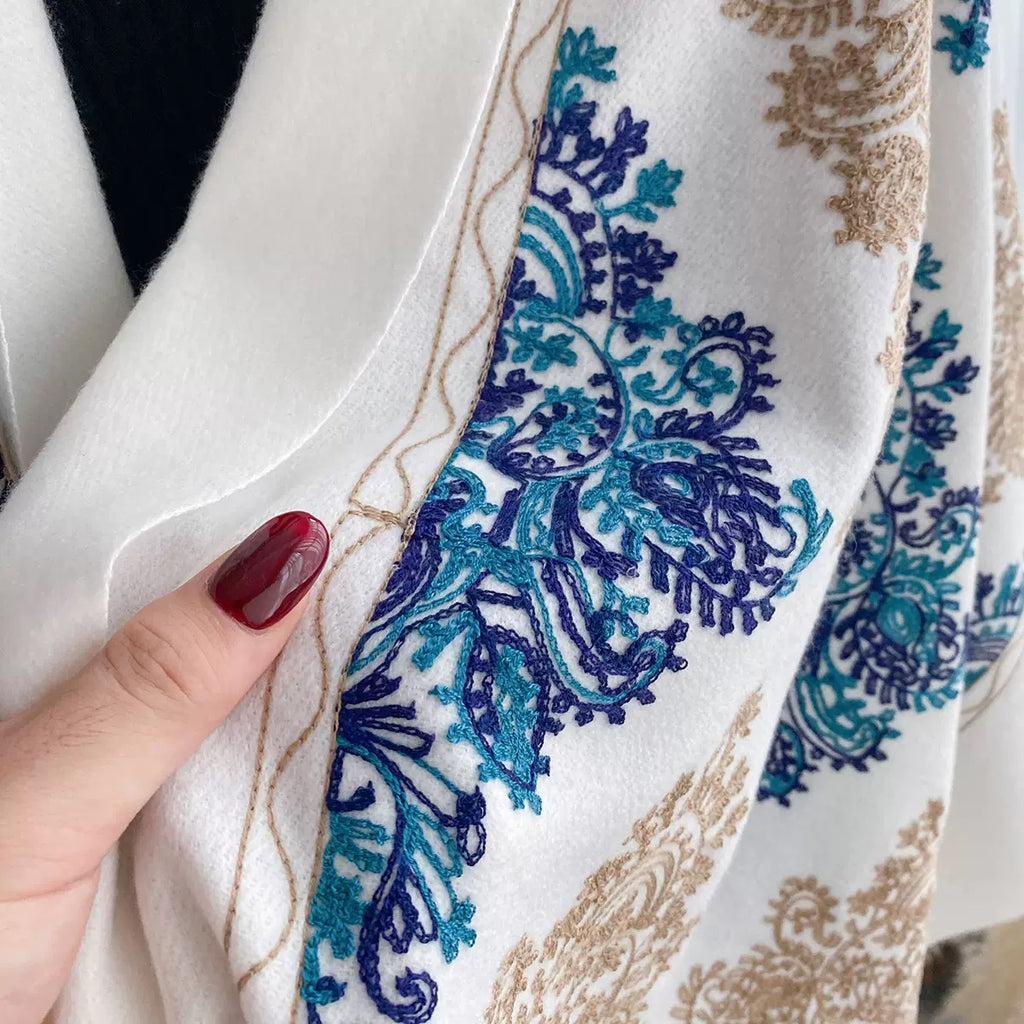 Close-up of Bohemian Elegance Winter Scarf with Fringe showing cobalt blue and teal embroidered paisley motif with golden chainwork thread detail on white faux cashmere
