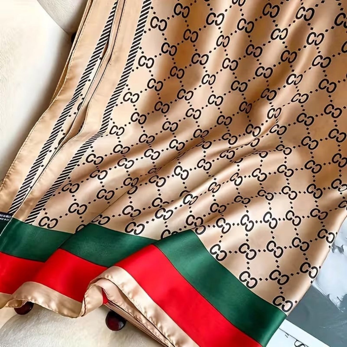 Beige silk scarf with black pattern and red and green stripes on a white surface