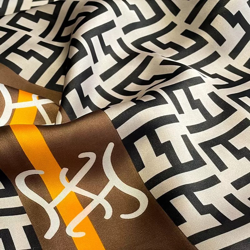 Designer geometric scarf fabric detail showing black white logo pattern and orange brown decorative border