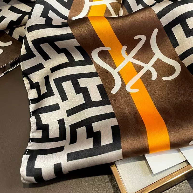 Close-up of designer logo print pattern and brown orange striped border detail on silk scarf