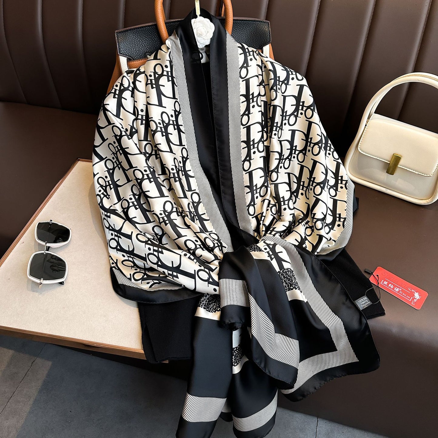 Black and white patterned scarf on a hanger with sunglasses and a handbag in the background.