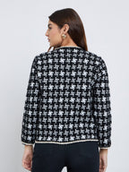 Back view of a black and white geometric knit cardigan for women with full sleeves and contrast braided hem trim.