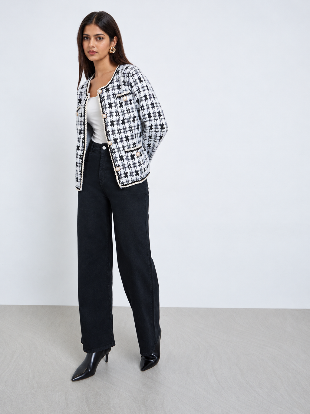 Women’s ivory and black geometric cardigan styled with black trousers, featuring pearl-effect buttons and elegant braided trim.