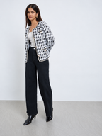 Women’s ivory and black geometric cardigan styled with black trousers, featuring pearl-effect buttons and elegant braided trim.
