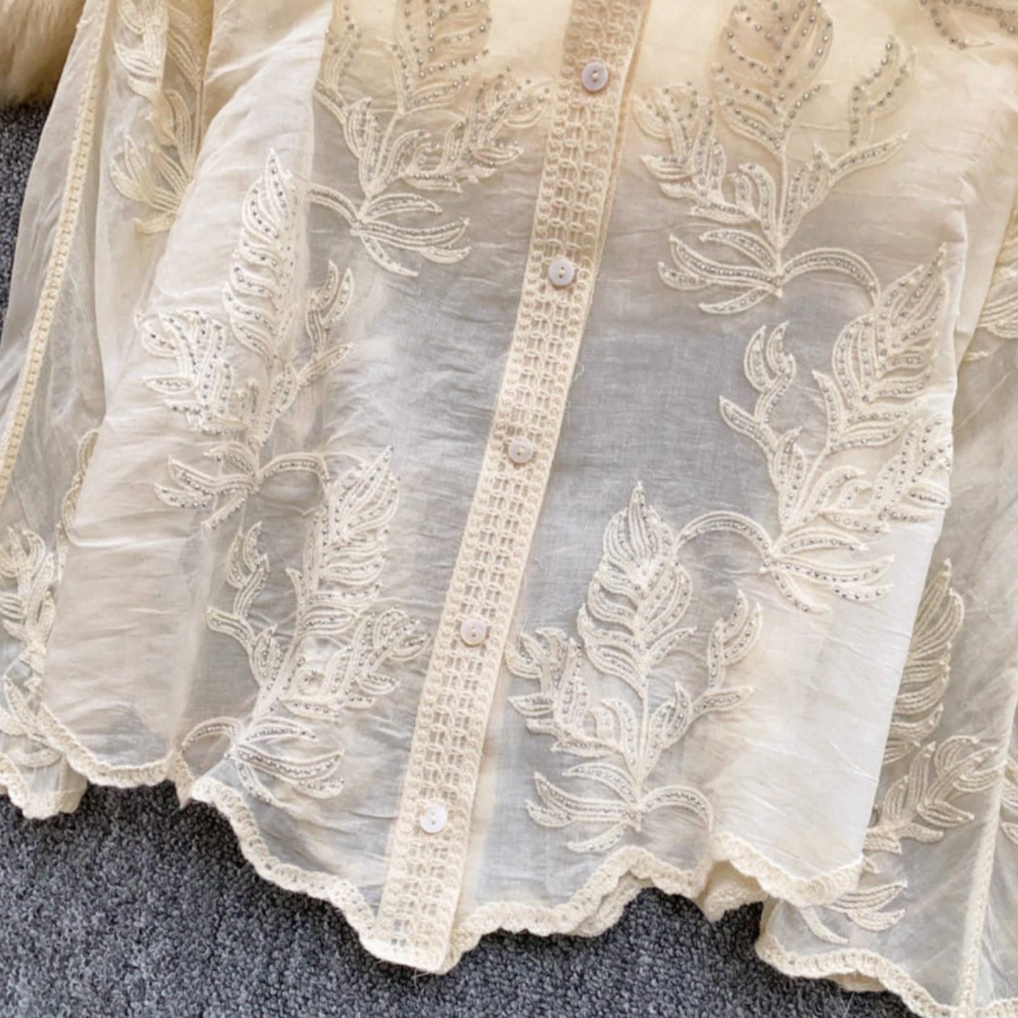 Close-up of intricate floral embroidery and lace detailing with silver embellishments on linen cotton shirt