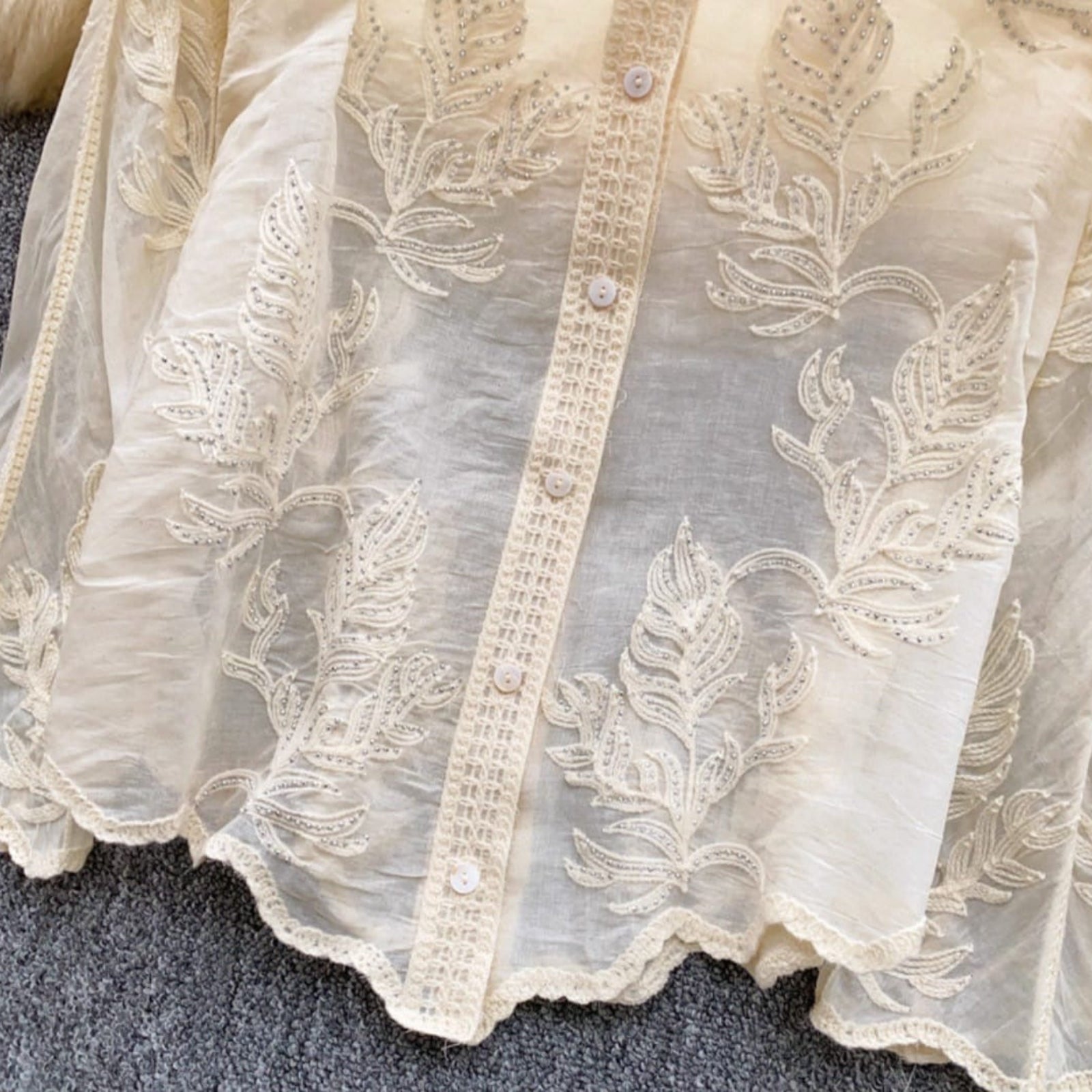 Close-up of intricate floral embroidery and lace detailing with silver embellishments on linen cotton shirt