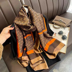 Patterned scarf held by a hand with a magazine and sunglasses on a table in the background.
