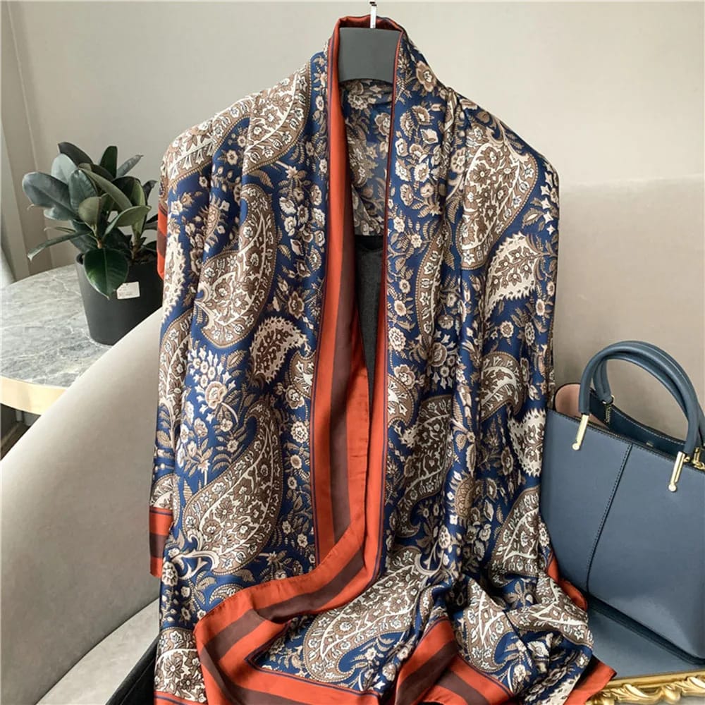 Gia Luxurious Paisley Print Silk Scarf in navy blue with intricate paisley motifs and rust satin border displayed in a flat lay.