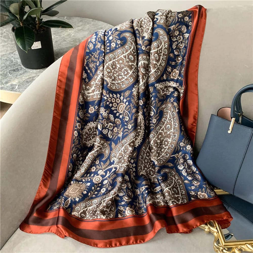 Gia Luxurious Paisley Print Silk Scarf featuring an elegant navy paisley print and rust border showcased on a hanger.
