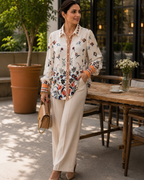 Woman wearing Jardin Bloom Satin Shirt in cream with botanical floral print, styled with wide-leg cream trousers and nude heels

