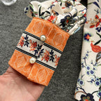 Close-up of Jardin Bloom Satin Shirt showing structured orange contrast cuff with pearl buttons and floral border print detail
