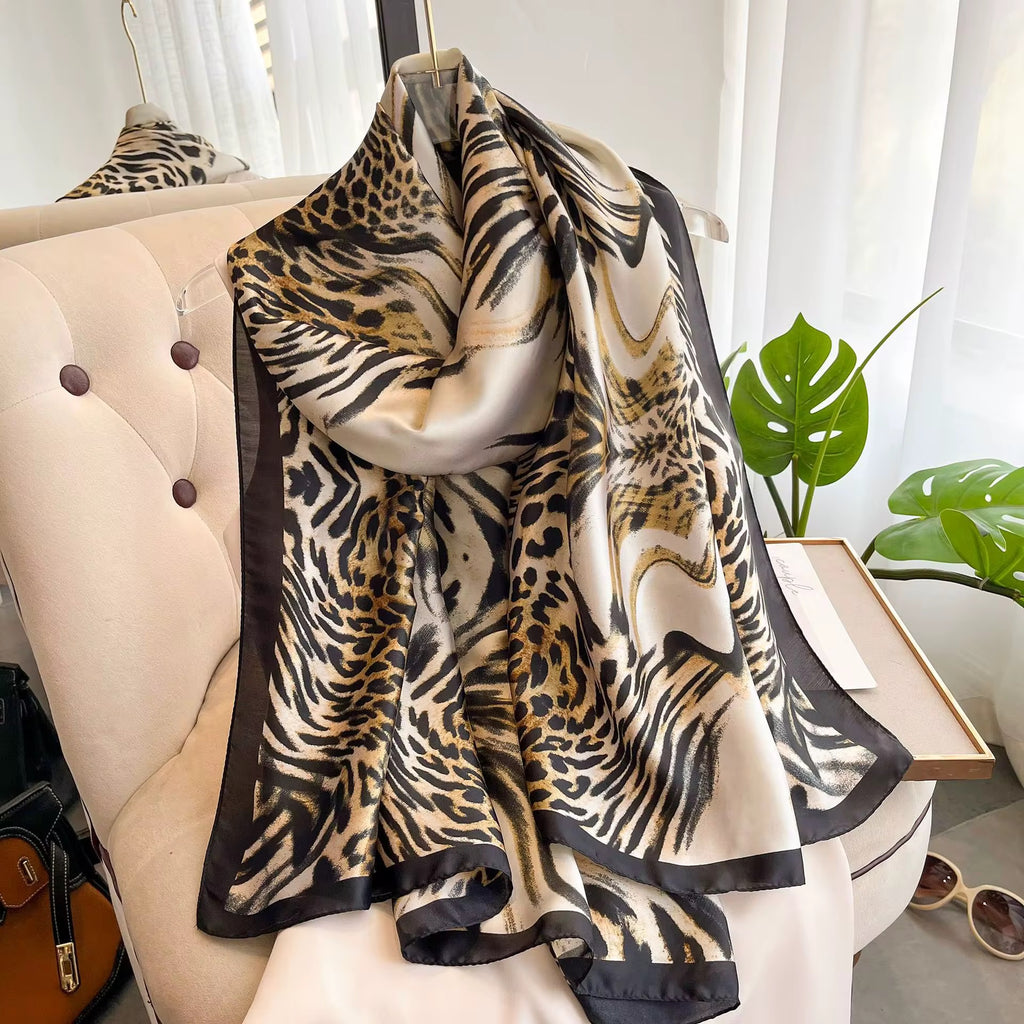 Luxe Savannah Silk Scarf draped over cream sofa showing leopard and zebra mixed animal print with black border
