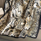 Close-up of Luxe Savannah Silk Scarf showing mixed leopard and zebra animal print texture with gold accents and black border
