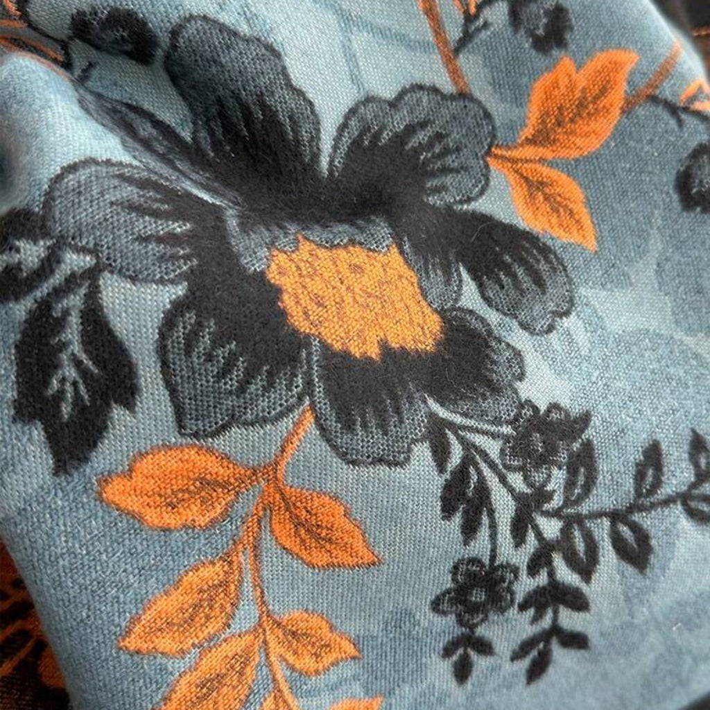 Close-up of Luxury Reversible Oversized Floral Shawl Wrap showing faux cashmere fabric texture with black floral motif and orange leaf detail on teal blue ground
