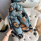 Luxury Reversible Oversized Floral Shawl Wrap held and gathered showing teal blue floral jacquard print with orange sunflower motifs and fringe edge

