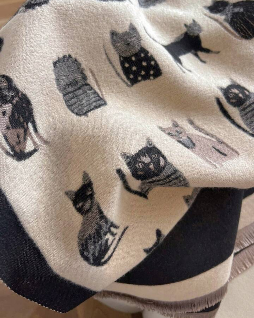 Close-up of The Midnight Cats Reversible Wrap showing soft faux cashmere fabric texture with detailed whimsical illustrated cat motif on midnight base

