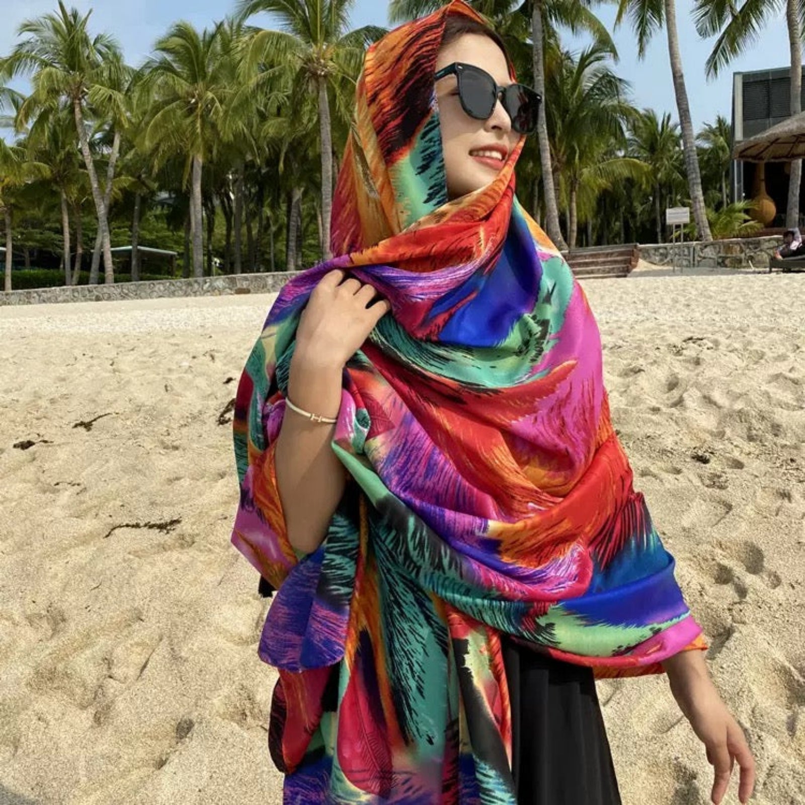 Woman wearing vibrant multicolor feather print stole at beach - summer resort scarf styling