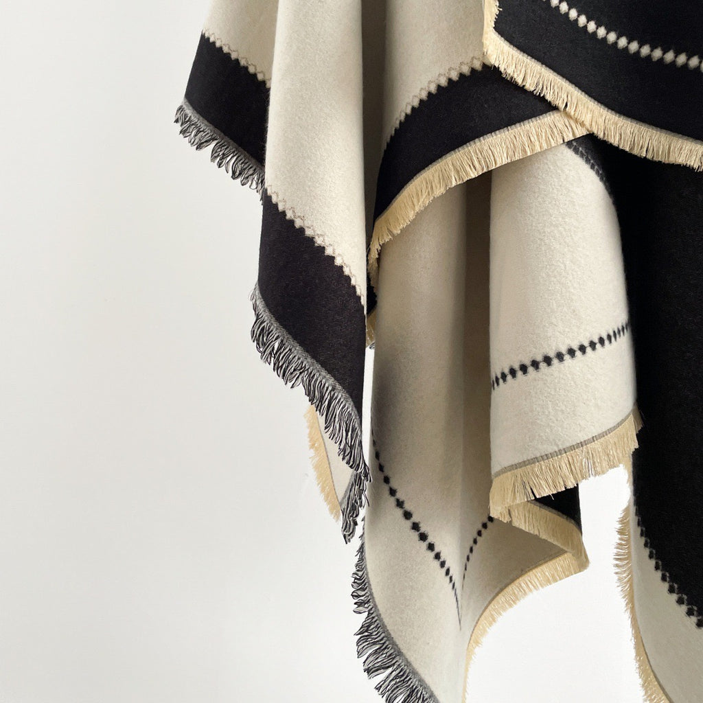 The Noir Geometry Cashmere Cape laid flat displaying full geometric print in contrasting tones on deep black faux cashmere fabric
