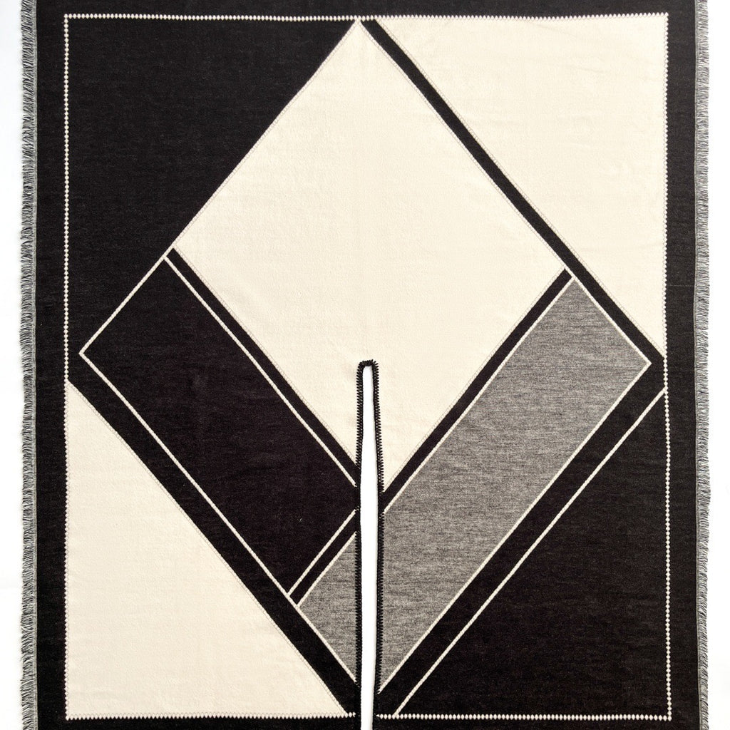 Close-up of The Noir Geometry Cashmere Cape showing soft faux cashmere fabric texture with bold geometric print detail in contrasting tones on noir black base
