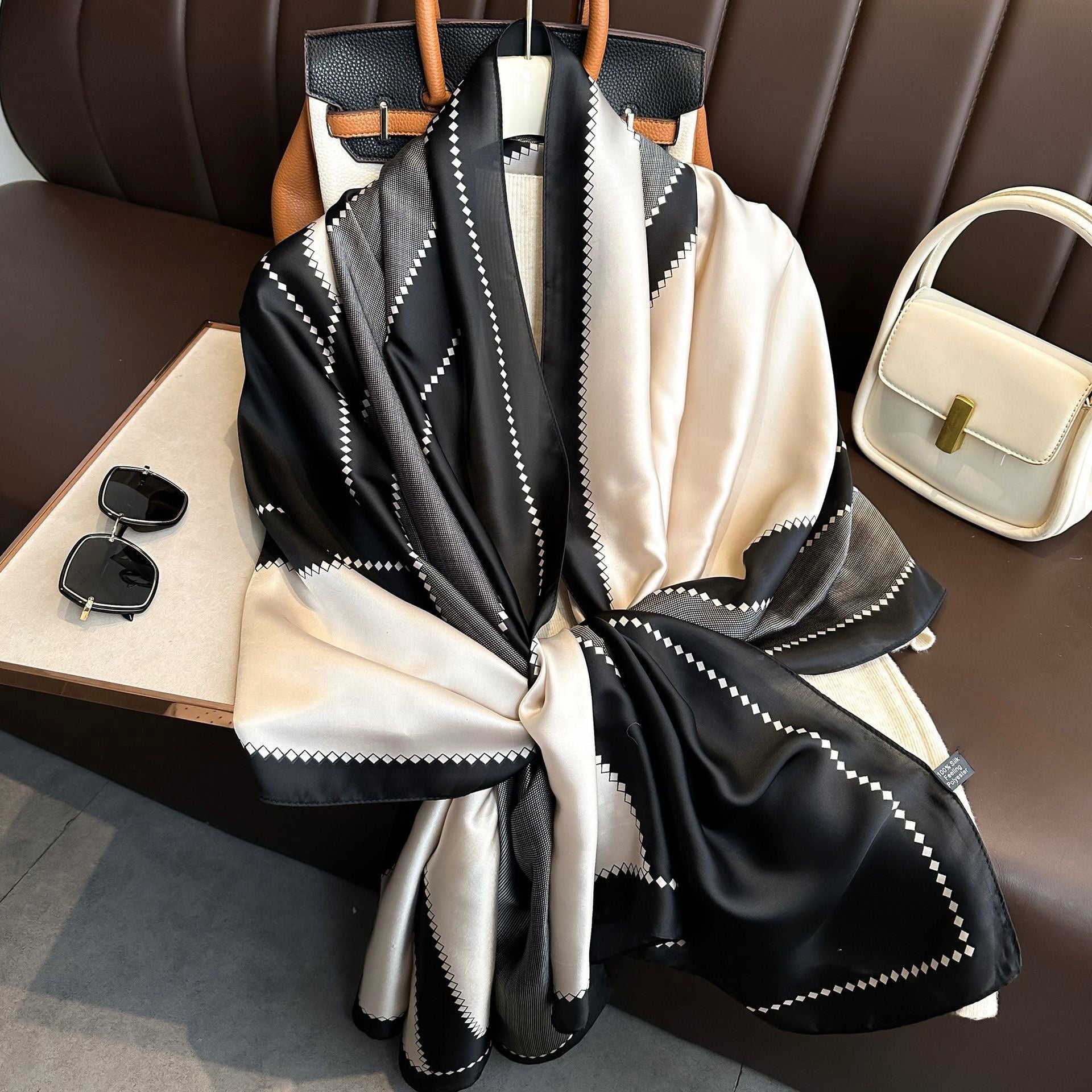 The Duchess Diamond Silk Stole in black, ivory and grey geometric diamond print, luxury satin silk scarf displayed on a handbag.