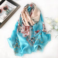 The Westery Blooming Garden luxury silk scarf gently folded to highlight its premium satin sheen, showcasing oversized pink peonies blooming against a vibrant sky blue and soft beige ombré background.
