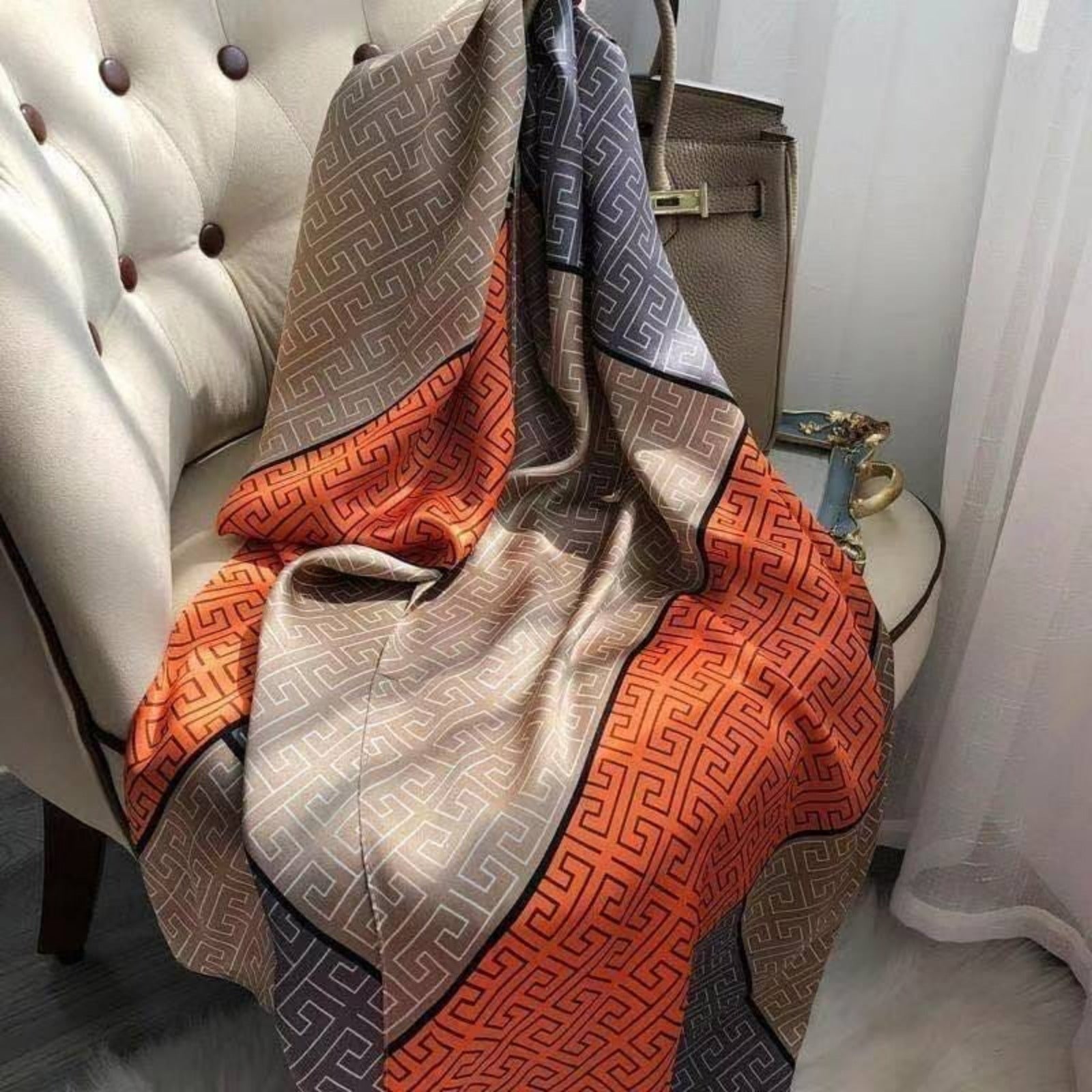 Premium satin silk-feel scarf with Greek key geometric print in taupe, charcoal grey and burnt orange, beautifully draped for luxury fashion styling.
