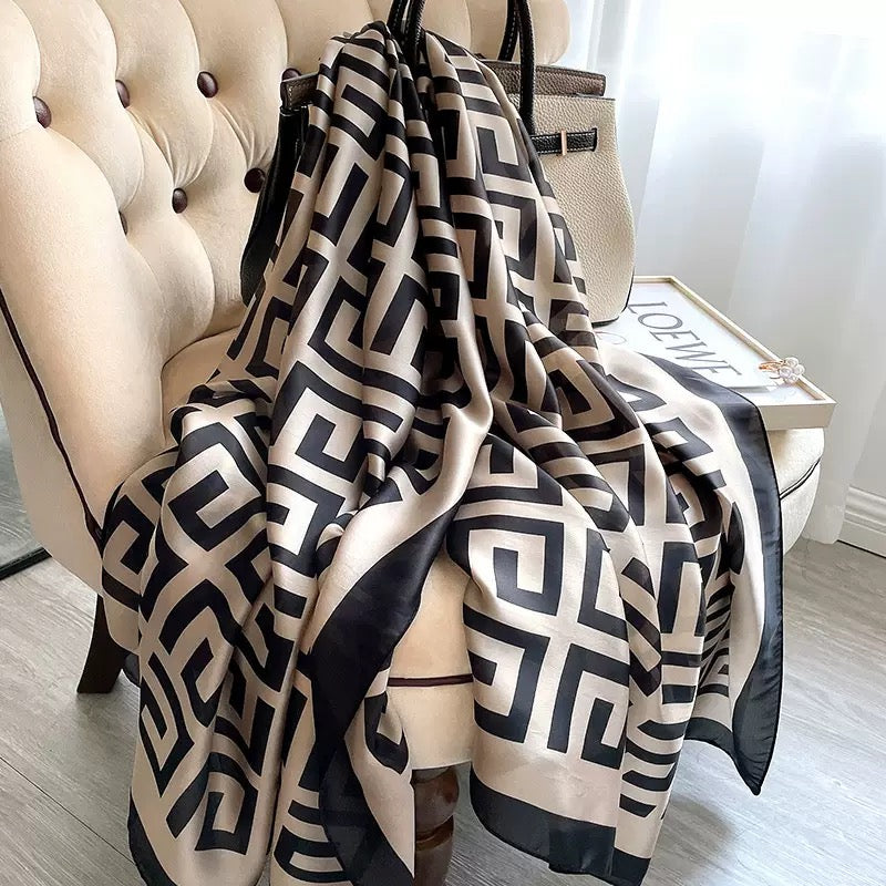 Grand Maze Graphic luxury silk stole by Westery draped elegantly over an armchair, showcasing its bold black geometric greek-key style pattern on a premium beige silk fabric.
