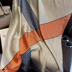 Flat lay of a luxury satin silk-feel scarf featuring a modern Greek key geometric print in taupe, charcoal grey and burnt orange.