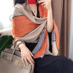 Woman wearing a premium imitation silk scarf with a Greek key geometric pattern in taupe, charcoal grey and burnt orange, styled as a luxurious wrap.