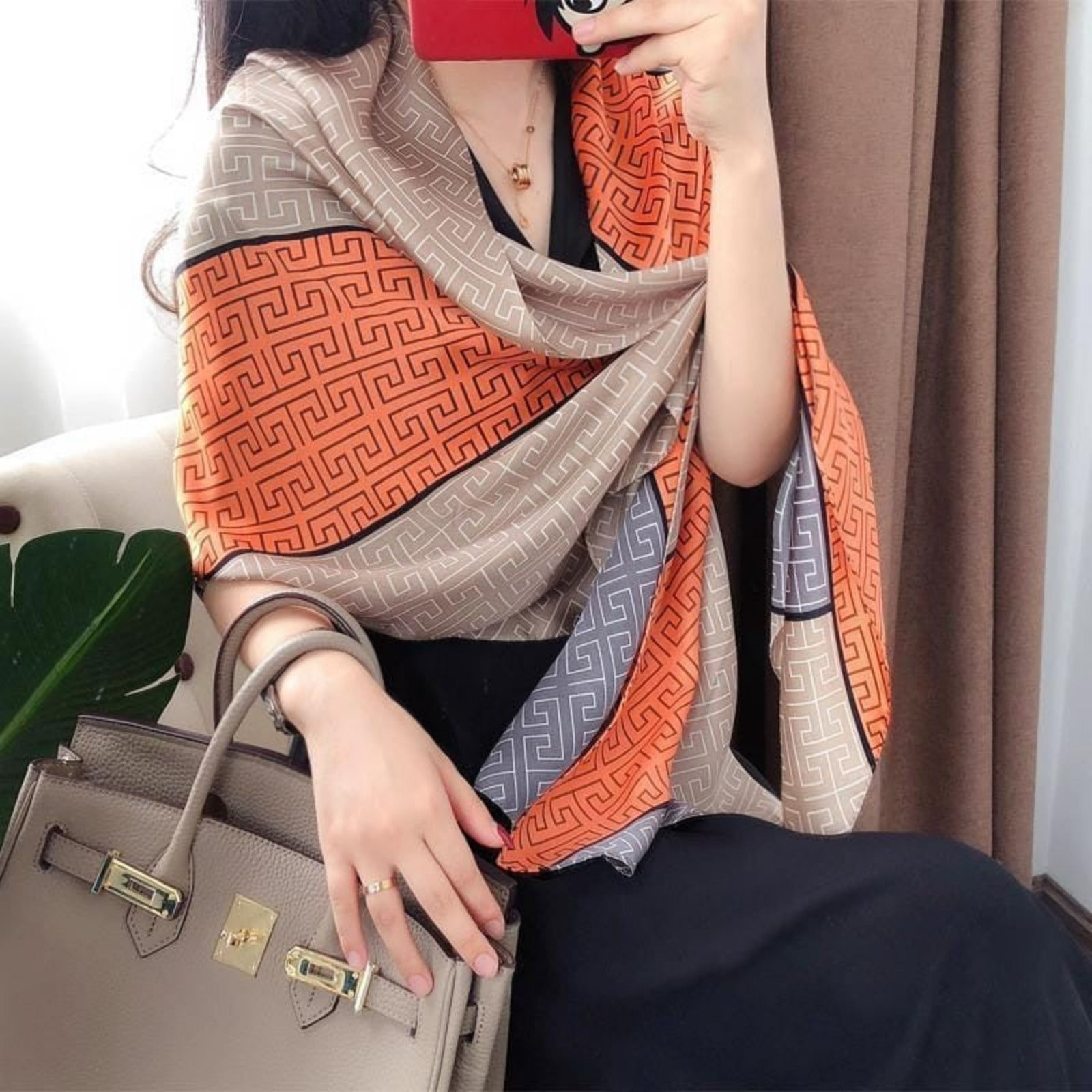 Woman wearing a premium imitation silk scarf with a Greek key geometric pattern in taupe, charcoal grey and burnt orange, styled as a luxurious wrap.