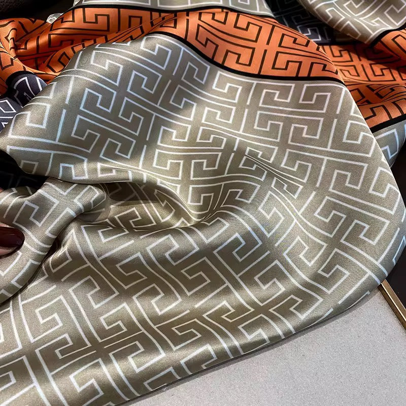 Close-up of the smooth satin silk-feel fabric showcasing the elegant Greek key geometric print in taupe, charcoal grey and burnt orange with a luxurious sheen.