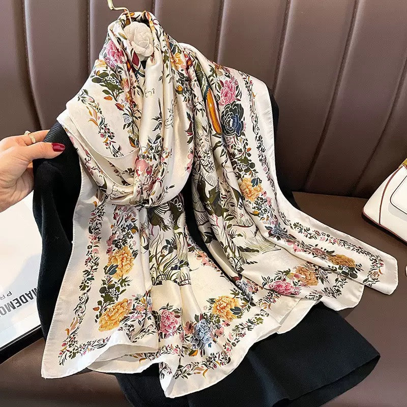 Imperial Garden Bird & Bloom luxury silk stole by Westery draped gracefully on a leather couch next to a premium handbag, showcasing its intricate botanical illustrations and vibrant floral patterns on soft ivory silk.
