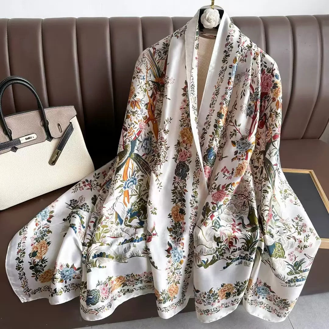 Westery Imperial Garden Bird & Bloom luxury silk scarf styled as a layered neck wrap on a hanger over a black blazer, emphasizing the rich contrast of multi-colored blossoms against a clean background.
