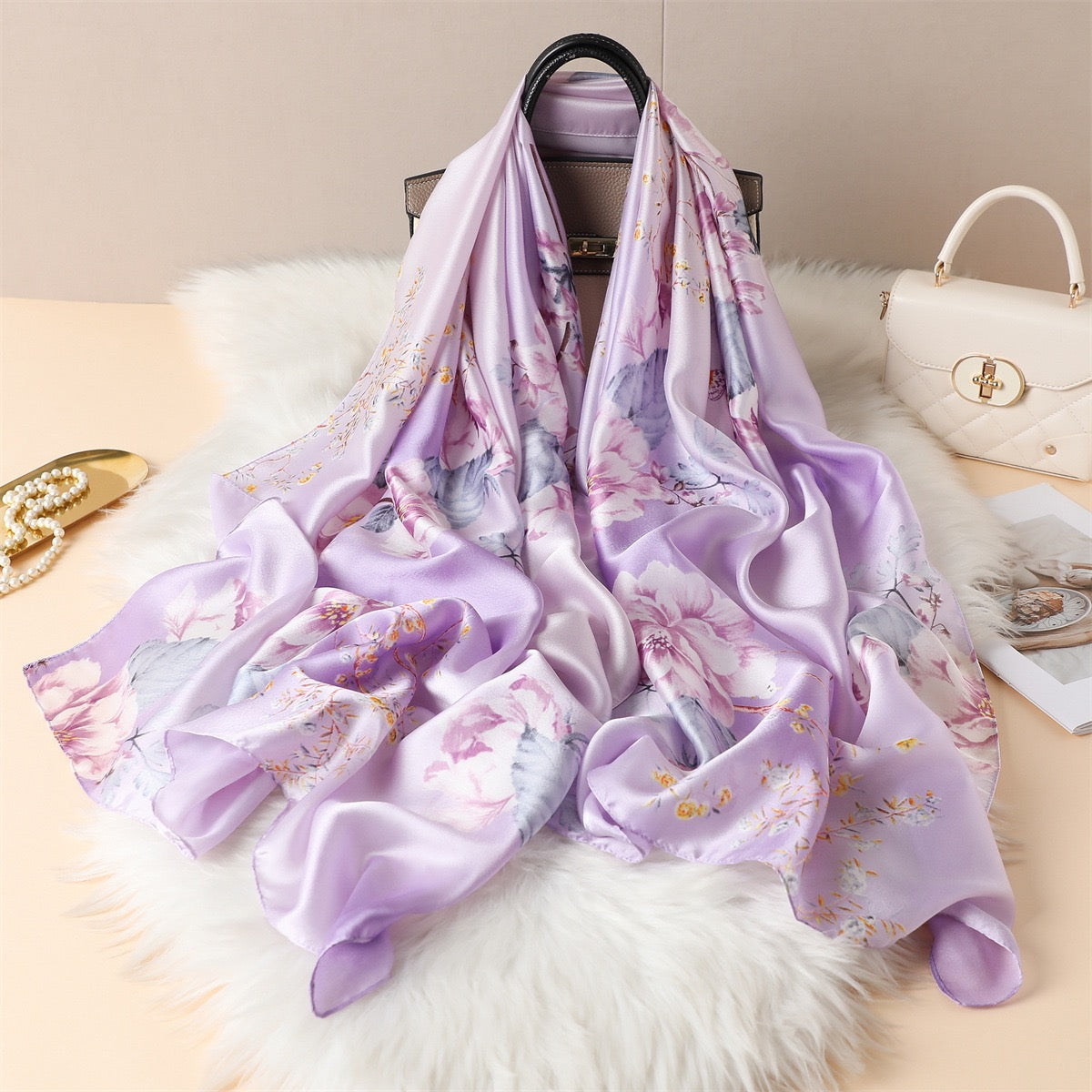 Lavender Magnolia luxury silk scarf by Westery cascading elegantly from a designer handbag onto a white faux fur rug, showcasing its premium satin luster and fluid, graceful drape.
