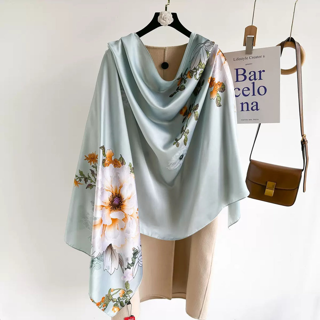 Westery Mint Blossom Garden premium silk scarf arranged in a flowing cowl style over a beige winter trench coat, demonstrating its elegant drape and subtle watercolor floral accent placement.
