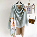 Westery Mint Blossom Garden premium silk scarf arranged in a flowing cowl style over a beige winter trench coat, demonstrating its elegant drape and subtle watercolor floral accent placement.
