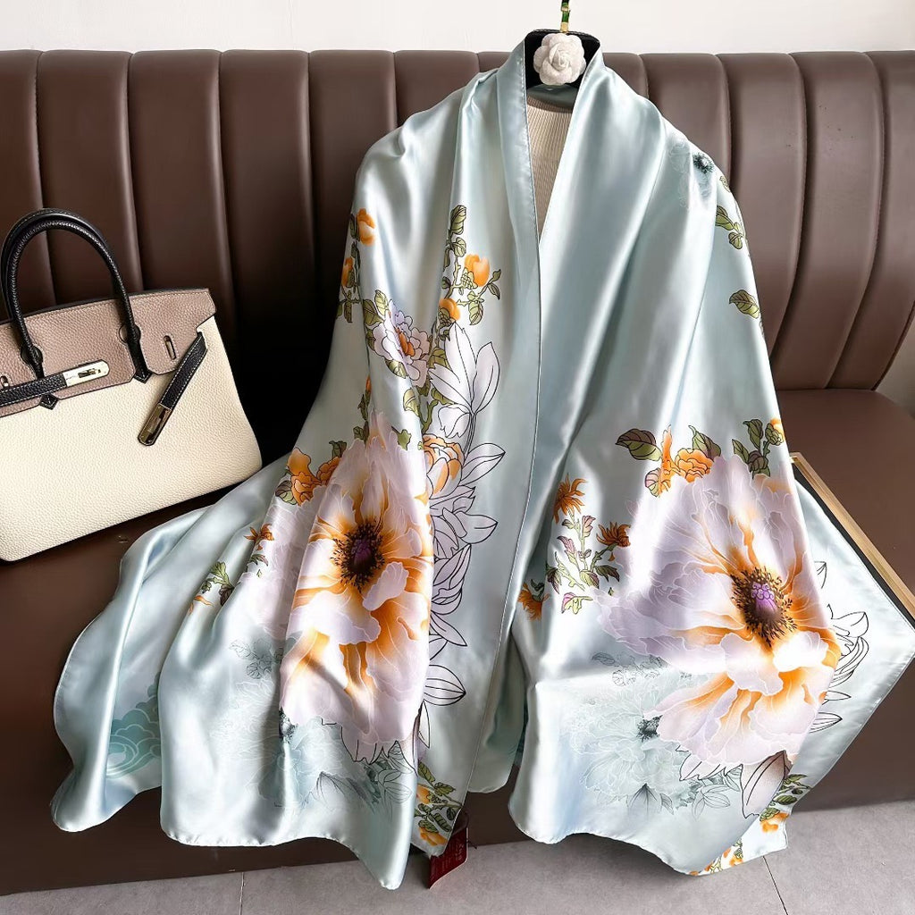 Mint Blossom Garden luxury silk stole by Westery draped gracefully over a leather sofa next to a designer handbag, showcasing oversized pastel orange and white peony blooms against a soft mint green background.
