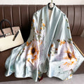 Mint Blossom Garden luxury silk stole by Westery draped gracefully over a leather sofa next to a designer handbag, showcasing oversized pastel orange and white peony blooms against a soft mint green background.
