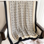 Full layout of the Westery Noir Lattice Monogram lightweight scarf draped over an armchair, highlighting the seamless repeating pattern, thin tan accent lines, and solid black frame.
