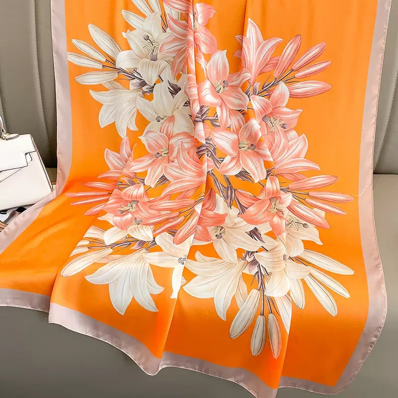 Westery Sunkissed Lily orange floral silk stole styled with a chic front knot on a hanger, highlighting its elegant drape and contrasting neutral border.
