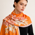 Sunkissed Lily luxury silk stole by Westery, featuring a vibrant orange fabric with an elegant white lily floral pattern and a neutral border close up worn by a model 