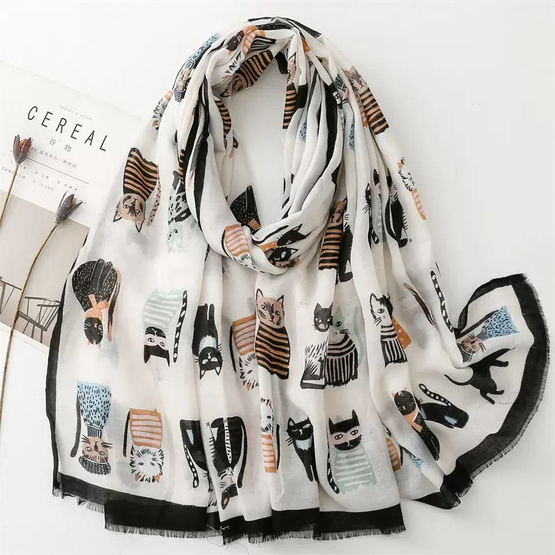 Whisker Tales premium viscose cotton stole by Westery draped naturally, featuring a whimsical array of illustrated cats in stripes, polka dots, and sweaters against a soft off-white background with a fringed black border.

