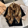 Wild Luxe Leopard luxury silk stole by Westery styled in an elegant drape on a hanger, showcasing its bold animal print pattern, rich golden-brown tones, and a solid black border.
